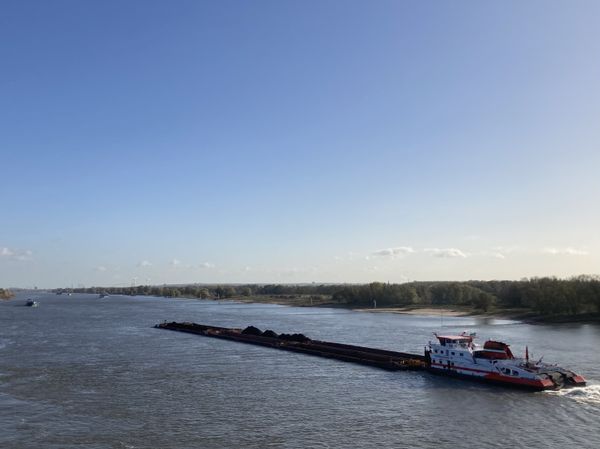 een schip vervoert kolen over de Waal, in de verte zijn windmolens te zien